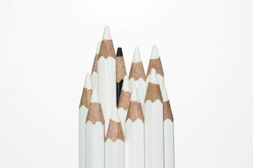 Several white pencils with one black pencil