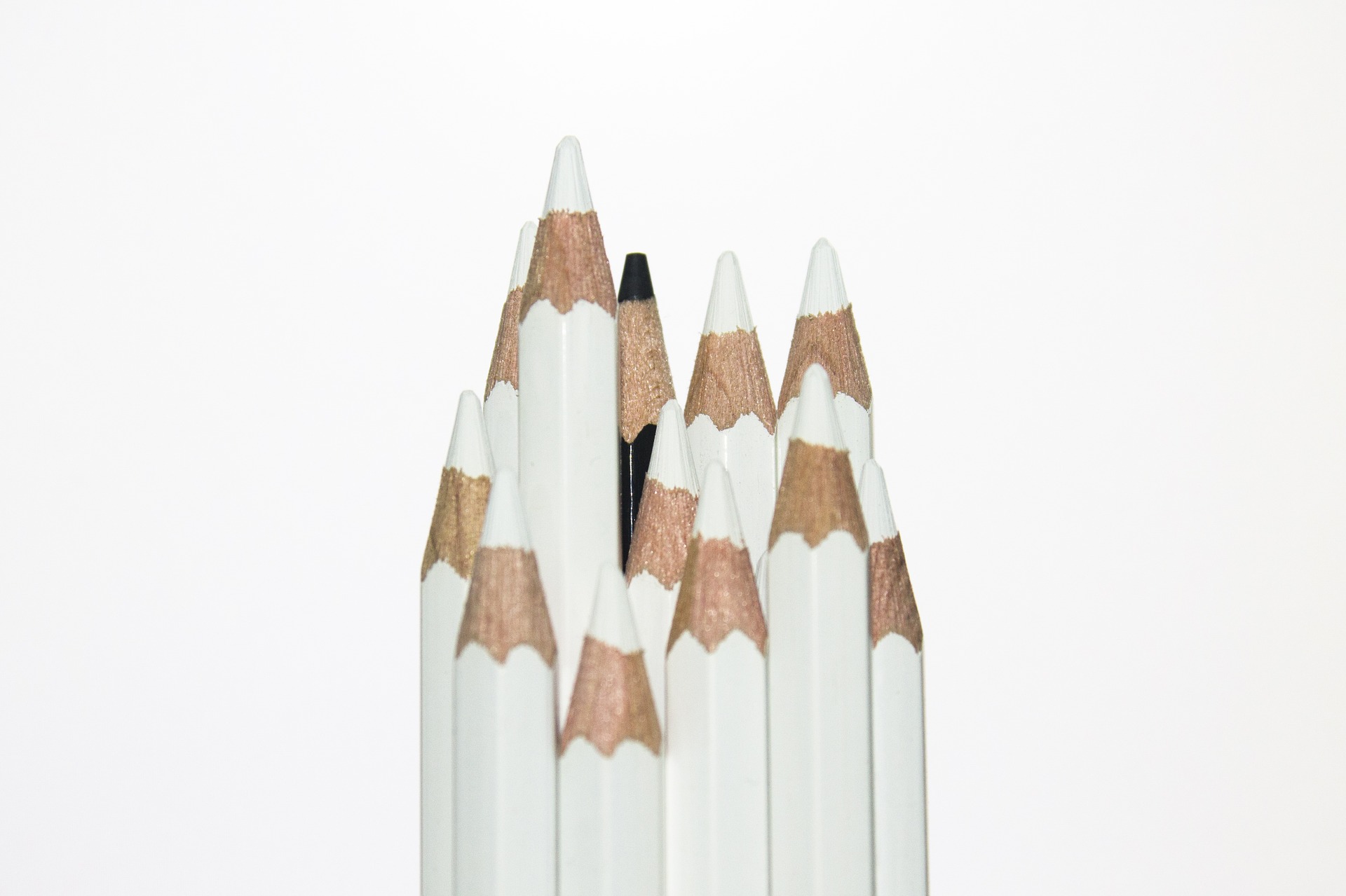 Several white pencils with one black pencil
